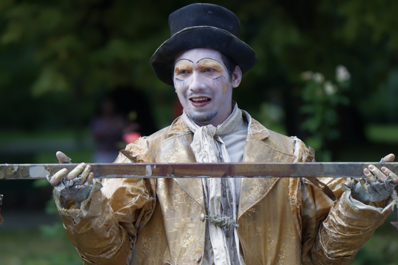 9 - A performer dressed as a living statue, featuring white face paint, a top hat, and a distressed gold coat